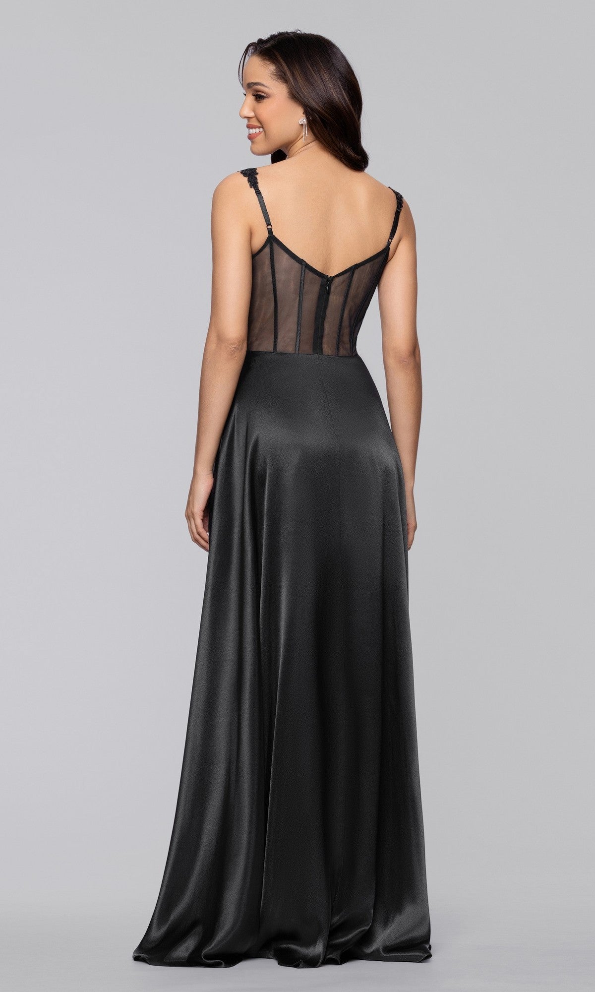 A woman, smiling and facing away from the camera, wears the Blondie Nites 6088BN—a long black satin a-line prom dress with thin straps and a sheer mesh back panel.